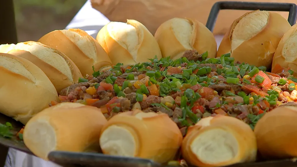 A foto mostra um Entrevero Gaúcho, com pedaços suculentos de carne bovina grelhada, Ao redor da carne, estão dispostos pães de sal.