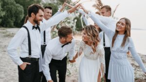 Um grupo alegre de pessoas na praia, levantando as mãos no ar com entusiasmo e felicidade durante uma cerimônia de casamento.