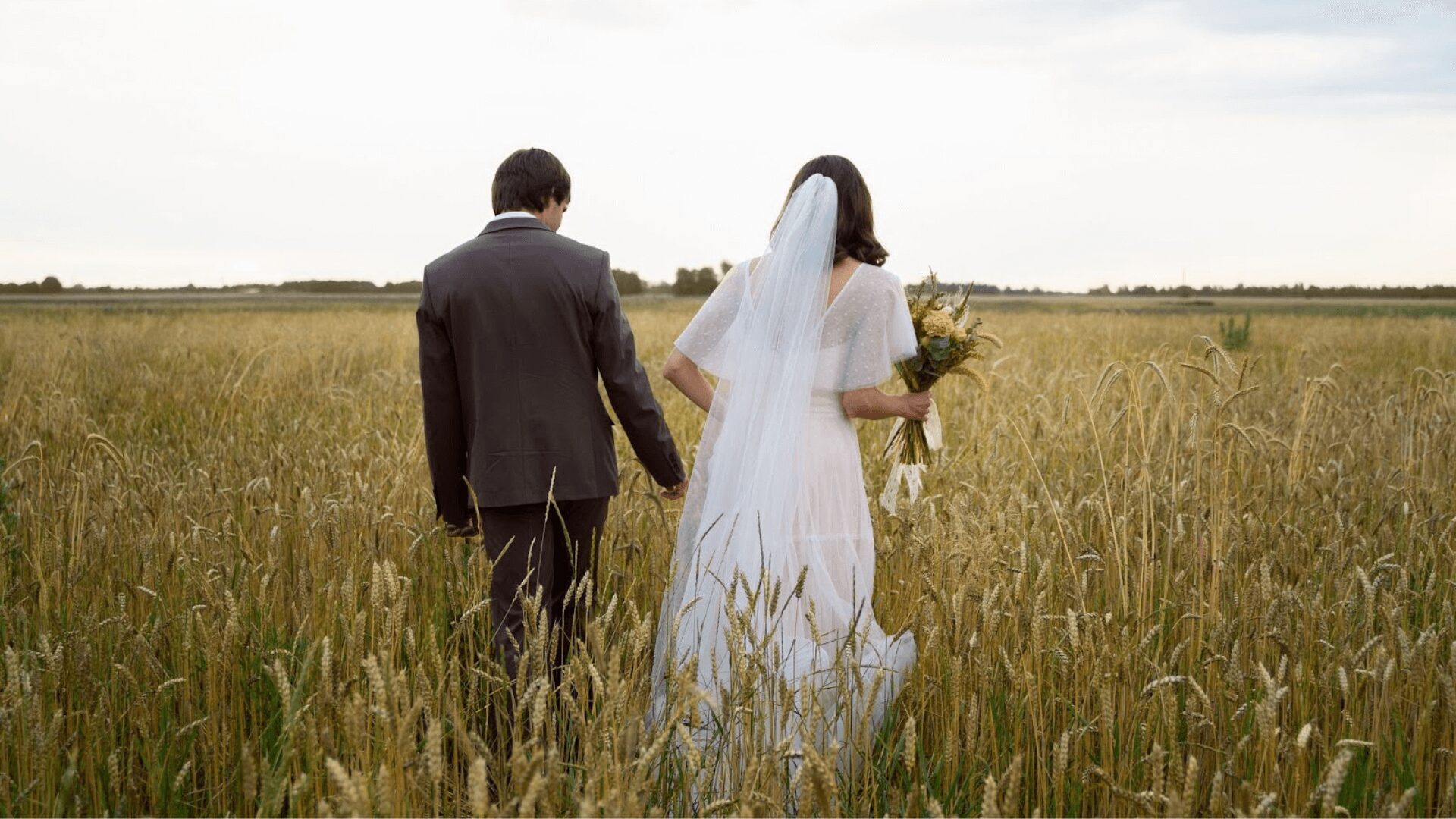 Um casal de noivos caminhando por um campo de trigo dourado. Um momento romântico e cheio de amor.
