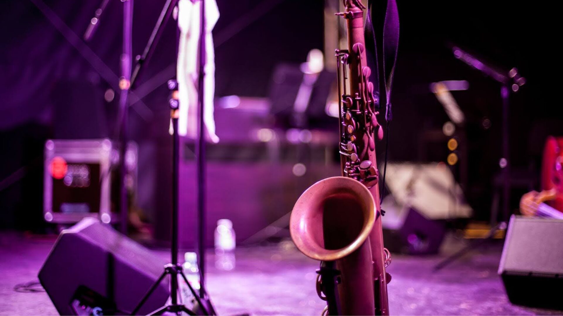 Um saxofone no palco junto a outros instrumentos e equipamentos.