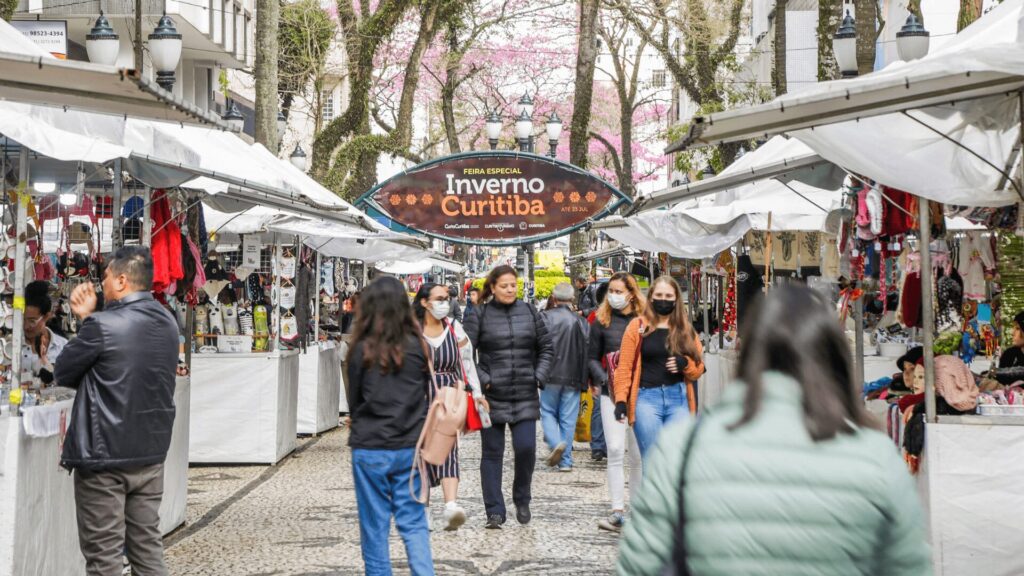 Pessoas caminham por uma feira à céu aberto com barracas e tendas.