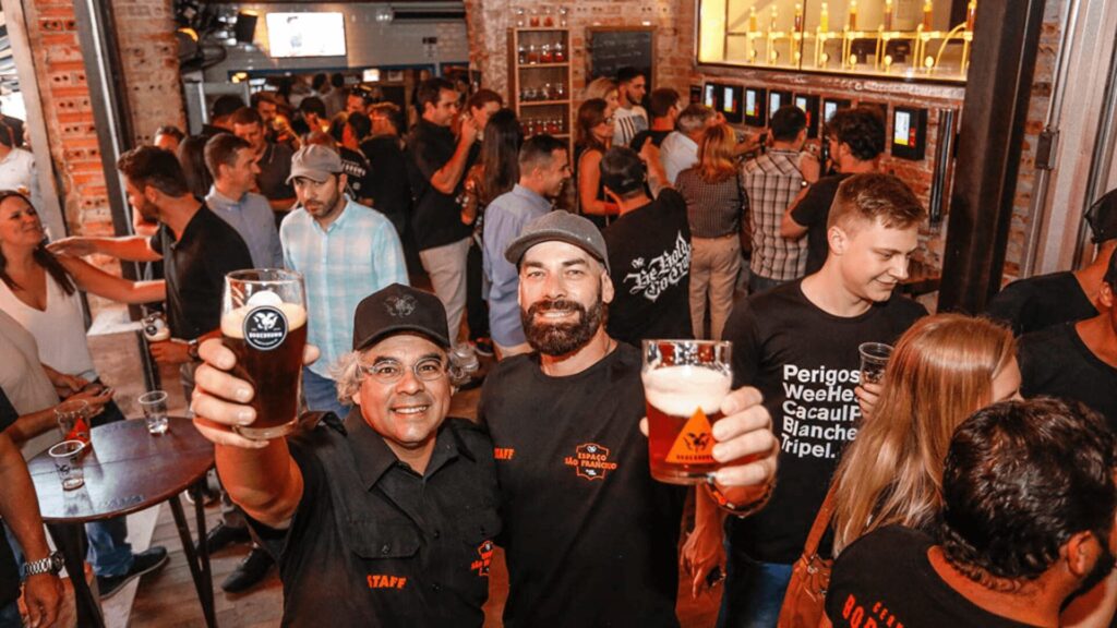 Dois homens de pessoas mostram copos de cerveja para a câmera em um bar.