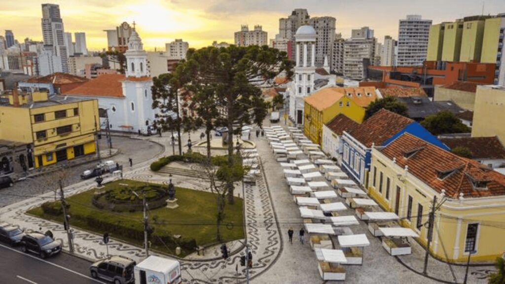 Paisagem urbana movimentada com prédios imponentes e uma cena de rua animada cheia de barracas de feira.