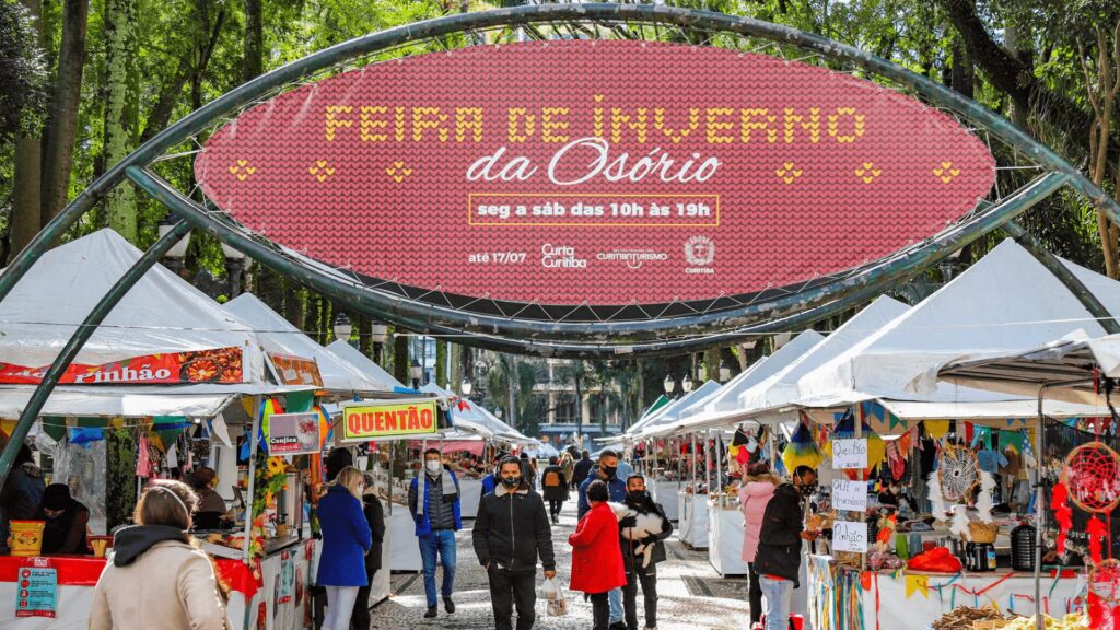 Um mercado de rua movimentado, com pessoas caminhando sob um arco, repleto de cores e atmosfera animada.