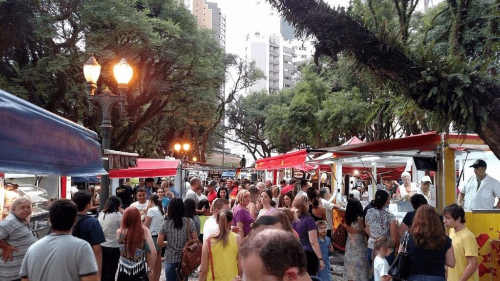 Uma cena movimentada de rua com pessoas desfrutando de comida e fazendo compras.