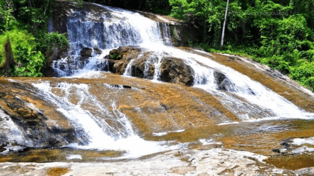 Uma belíssima cachoeira com água caindo em cascata, rodeada por vegetação.