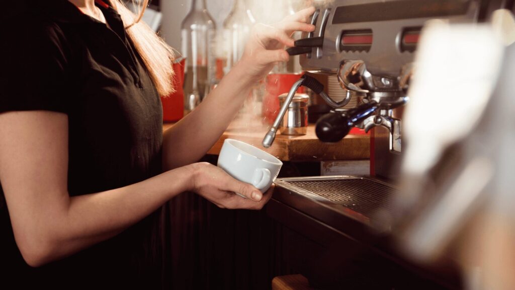 Uma barista mulher servindo café em uma xícara.