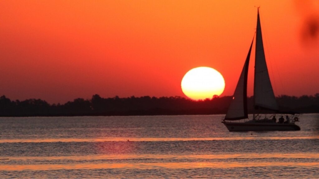 Um veleiro navega em um rio ao pôr do sol.