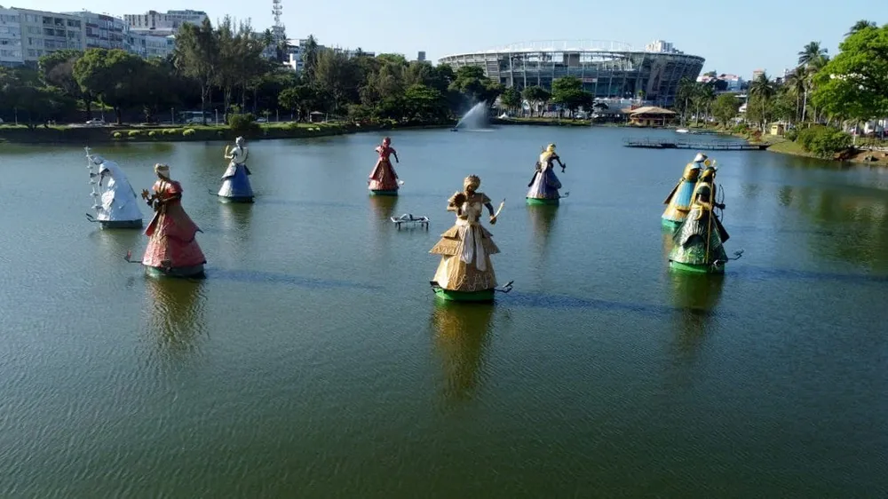 Grupo de estátuas em lago com construção ao fundo.