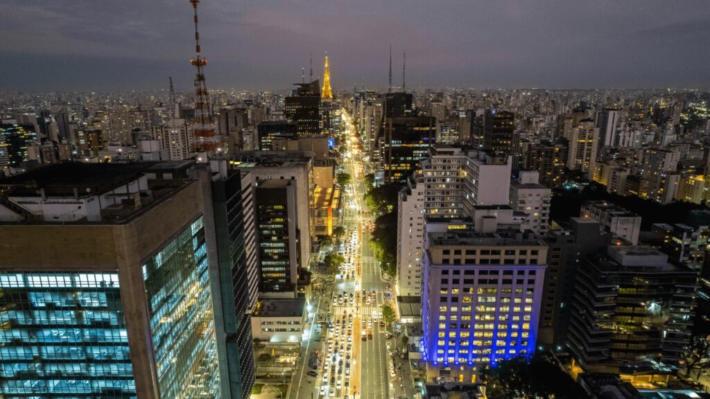 Vista aérea noturna de uma paisagem urbana movimentada com ruas iluminadas e edifícios densos.