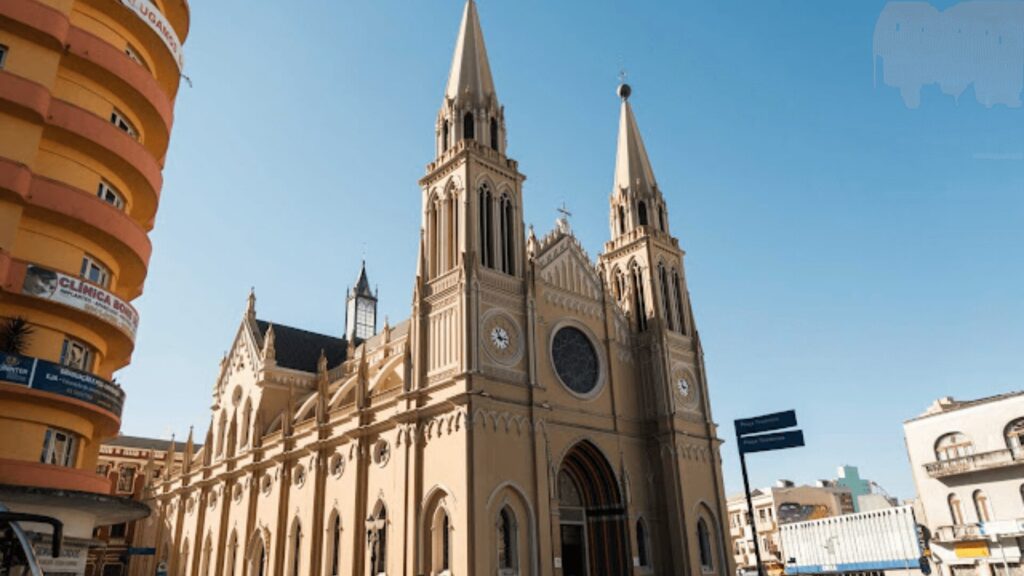 Fachada de uma igreja neo-gótica em um ambiente urbano, com pedestres e céu azul claro.