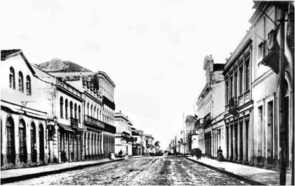 Foto histórica em preto e branco de uma rua vazia com edifícios vintage e um caminho molhado.