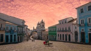 Cidade histórica com edifícios coloridos e estradas de paralelepípedos sob um céu rosa cheio de nuvens.