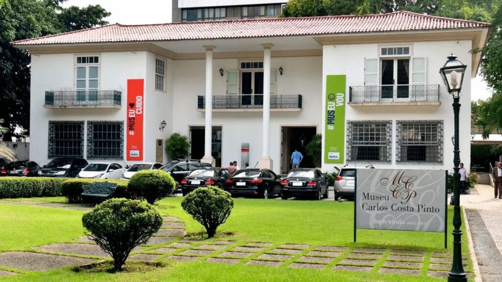 Edifício branco do museu em estilo colonial com banners e uma placa de boas-vindas.