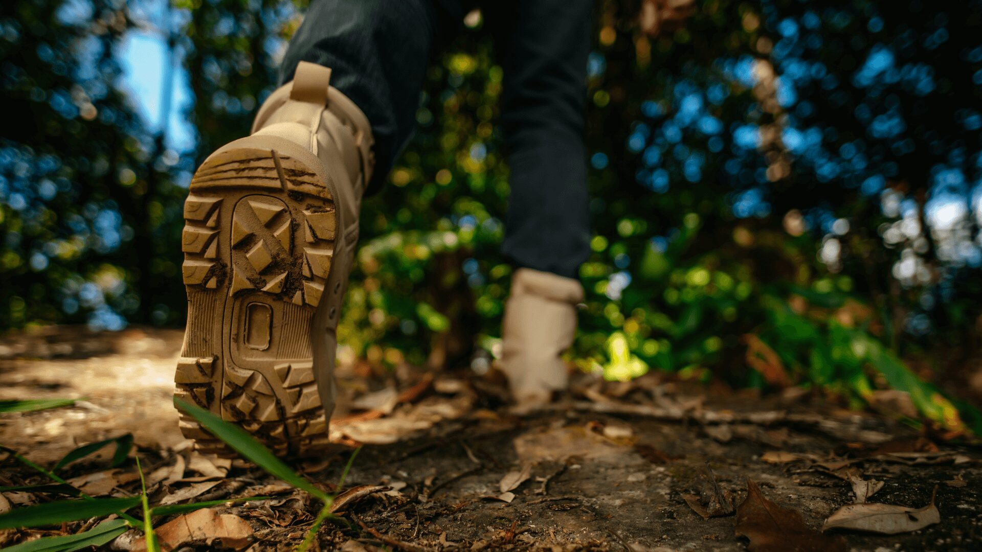 Pessoa caminhando na floresta, imagem com foco em botas pisando em uma trilha.