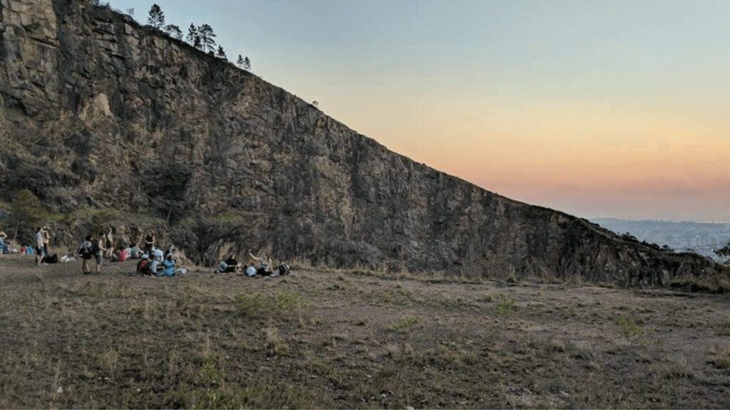 Pessoas relaxando na base de um penhasco íngreme durante o pôr do sol.