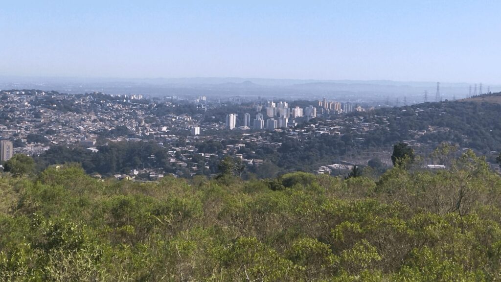 Uma vista panorâmica de uma extensa paisagem urbana com edifícios, cercada por vegetação e colinas.