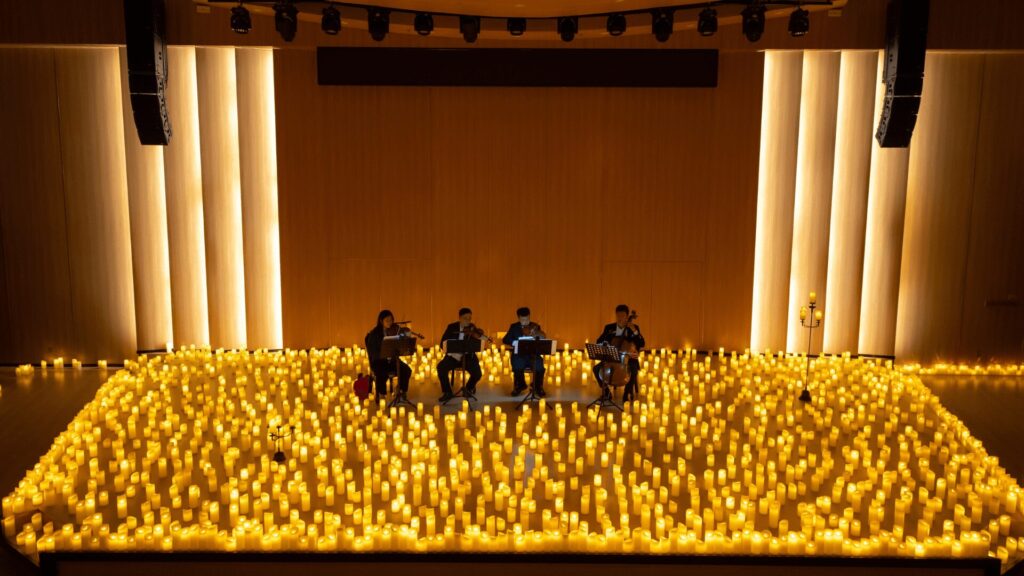 Quarteto de cordas tocando cercado por inúmeras velas acesas em um palco.