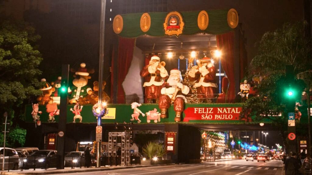 Uma decoração festiva de rua com vários Papais Noéis e um banner "Feliz Natal São Paulo".