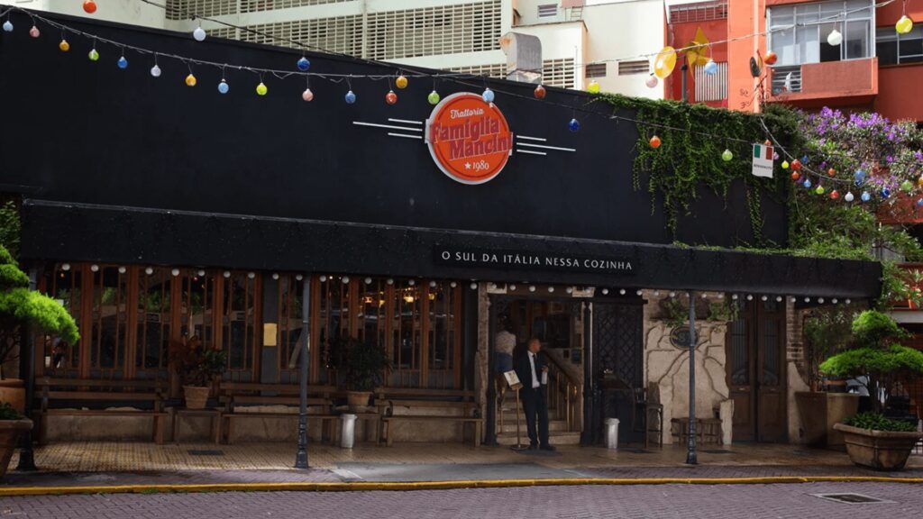 Fachada da Famiglia Mancini Trattoria, um restaurante italiano tradicional em São Paulo, com toldo preto, letreiro vintage e decoração aconchegante.