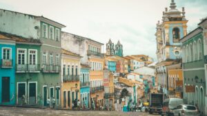 Edifícios coloniais coloridos em uma rua íngreme com uma igreja ao fundo e pessoas caminhando.