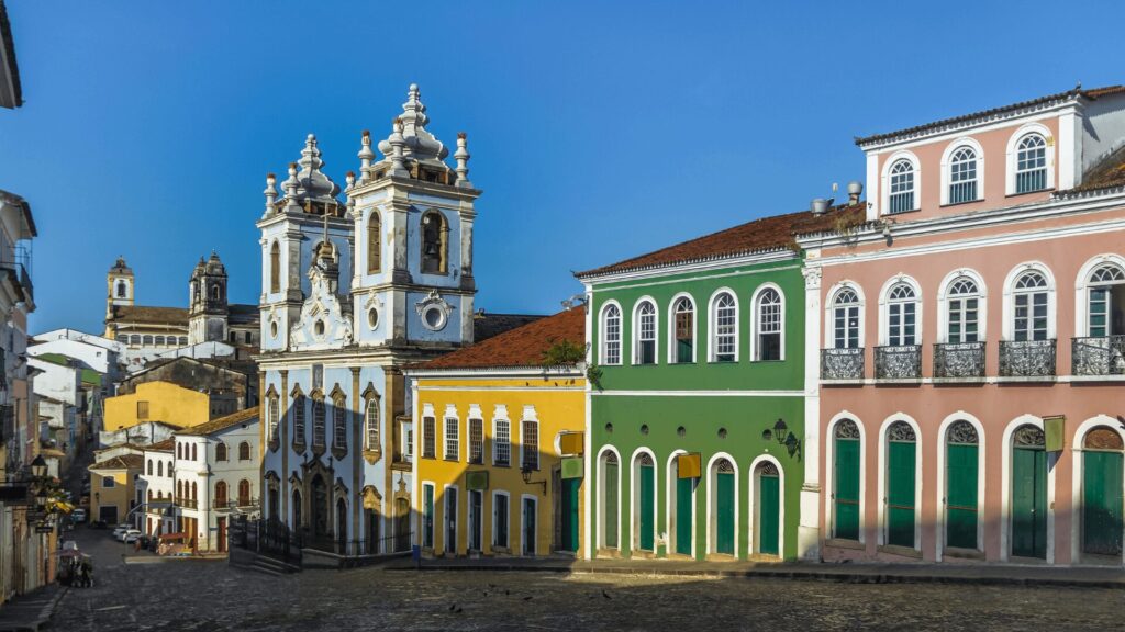 Edifícios coloniais em cores vibrantes com uma igreja barroca sob um céu azul claro. 