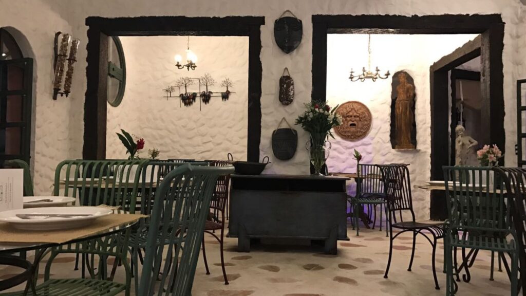 Interior de um restaurante aconchegante com paredes brancas texturizadas, decoração em madeira, móveis em estilo vintage e mesas florais.