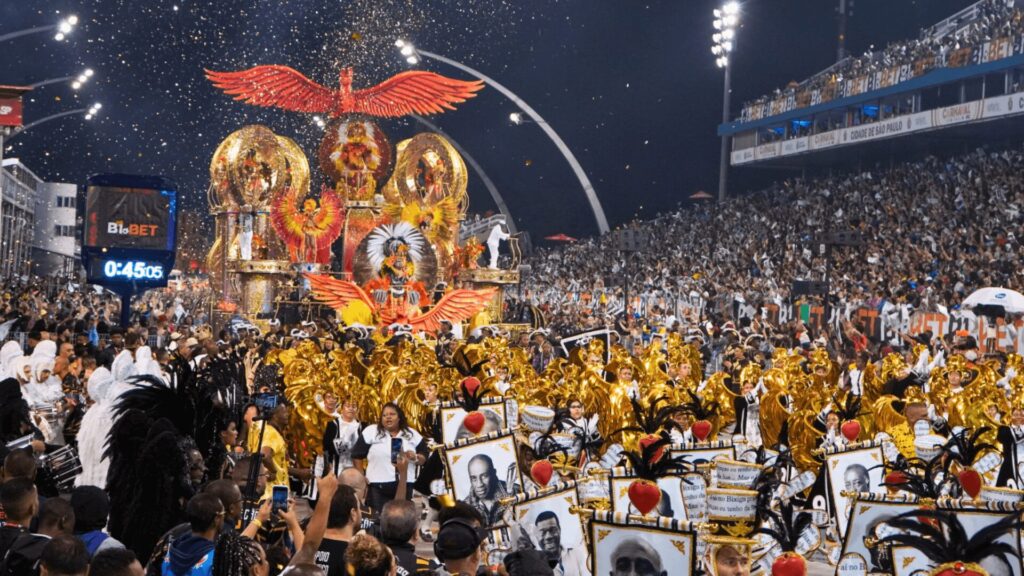 Um vibrante desfile de carnaval com carros alegóricos ornamentados, fantasias douradas e uma multidão animada, com confetes enchendo o céu noturno.