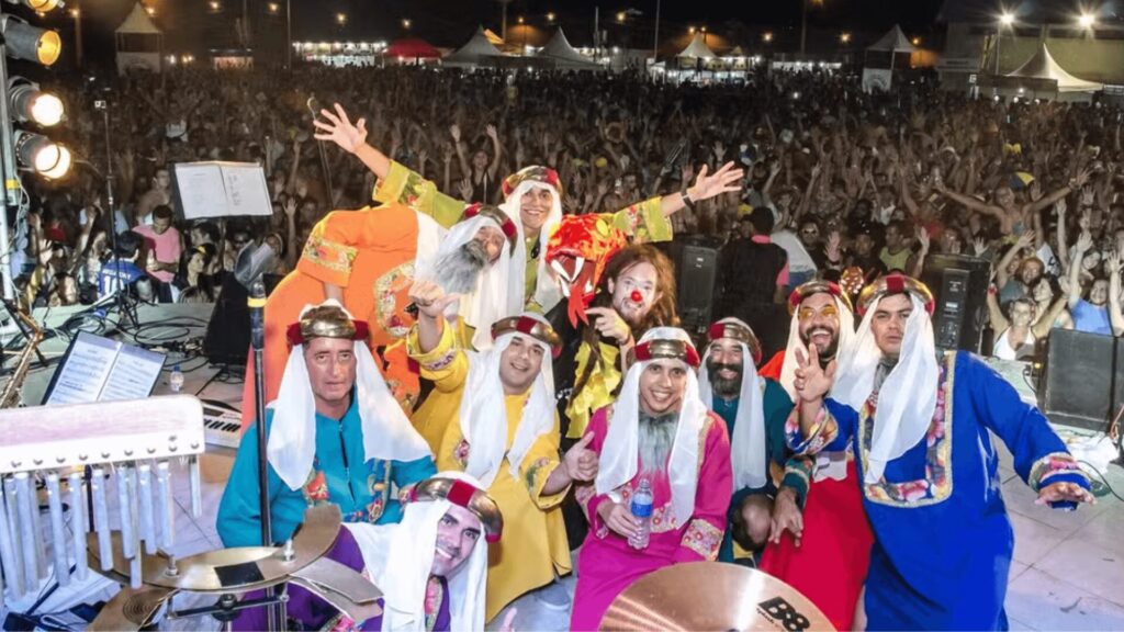 Uma multidão animada desfruta de uma apresentação enquanto artistas em trajes coloridos e tradicionais posam com entusiasmo no palco.