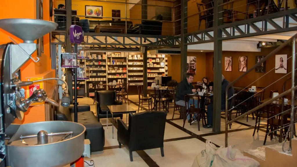 Uma cafeteria aconchegante com assentos de couro preto, mesas de madeira e uma exposição colorida de produtos de café nas prateleiras.