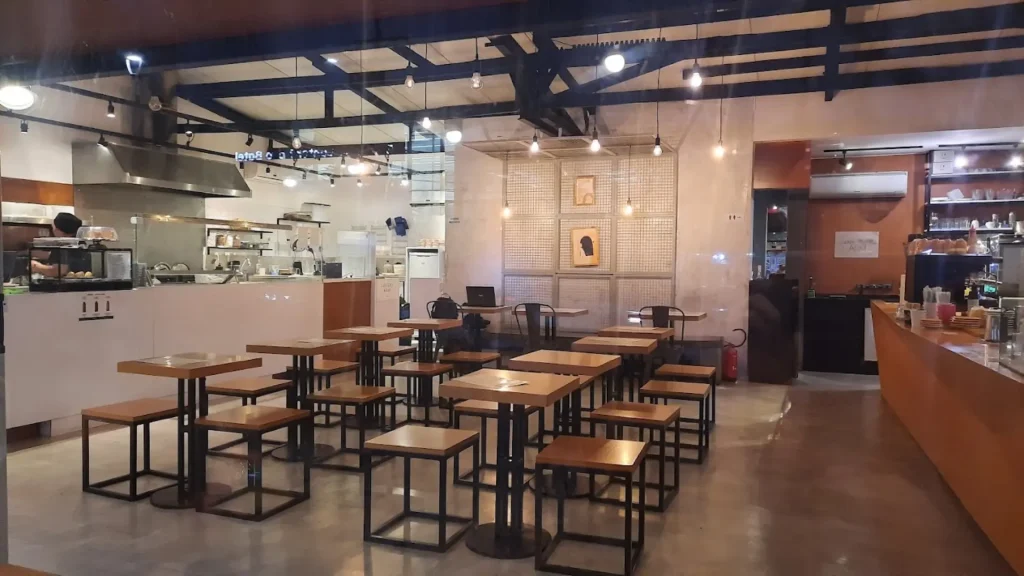 Interior de um café moderno com mesas de madeira, cozinha aberta e iluminação aconchegante, criando uma atmosfera acolhedora.