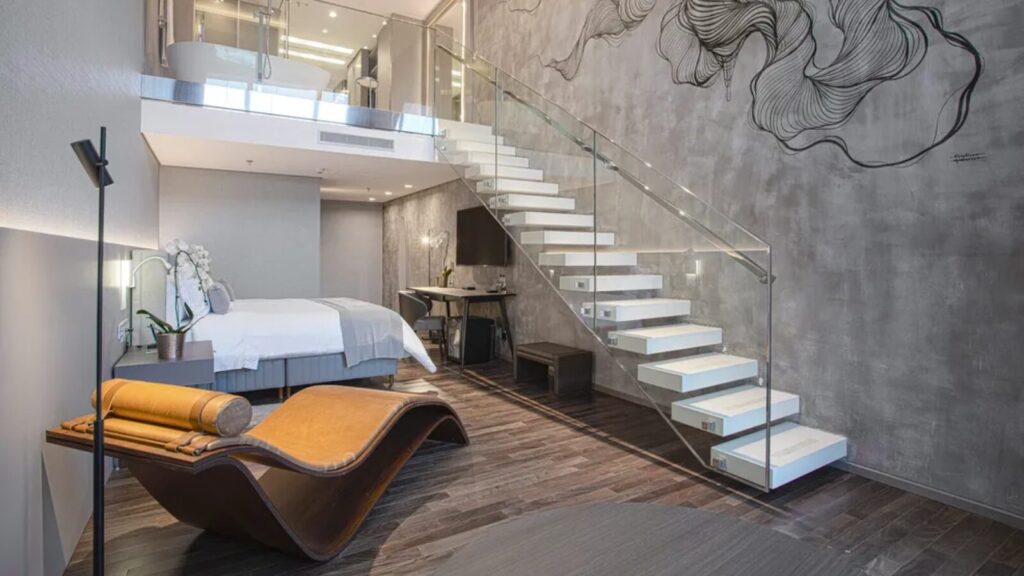 Suíte de hotel moderna com escada, móveis elegantes, cama confortável e design artístico nas paredes em um espaço estiloso.