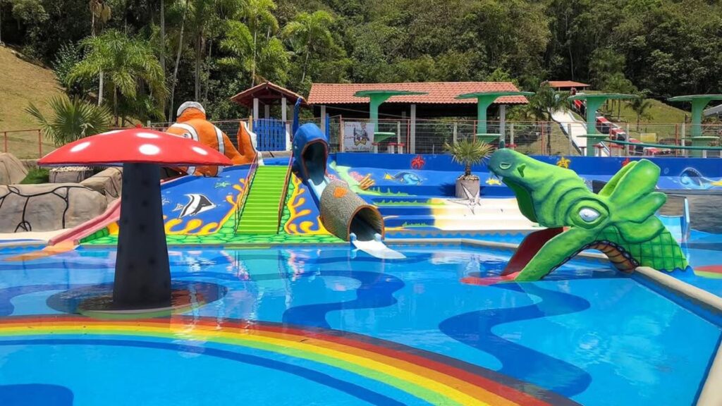 A imagem exibe um parque aquático vibrante e colorido, com várias atrações voltadas para crianças.